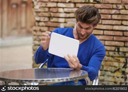 Young man using tablet pc as a mirror to fix his hair in outdoor cafe