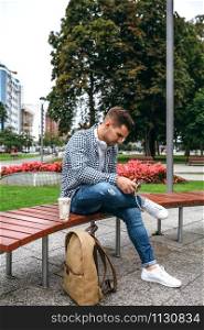 Young man using tablet sitting on a park bench outdoors. Young man using tablet outdoors