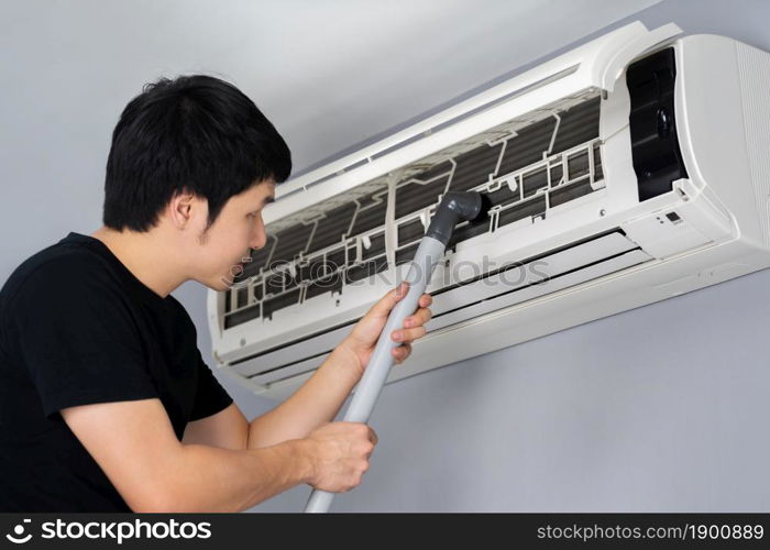 young man using vacuum cleaner to cleaning the air conditioner at home