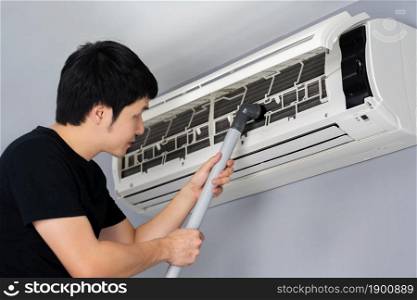 young man using vacuum cleaner to cleaning the air conditioner at home