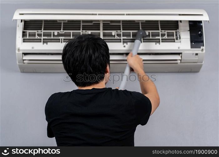 young man using vacuum cleaner to cleaning the air conditioner at home