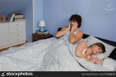 Young man waking up in bed while his wife sleeps. Man waking up while his wife sleeps
