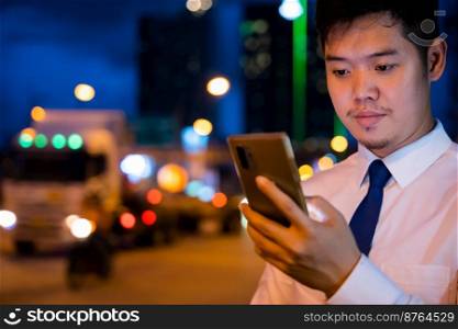 Young man walking and chatting on mobile phone with friends at social networks outdoor, Portrait Asian businessman typing an sms message via smartphone after work near office at night city street