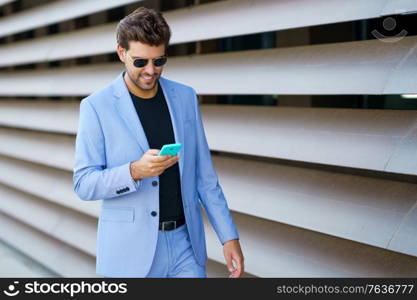 Young man walking down the street using his smartphone with a happy expression. Man walking down the street using his smartphone with a happy expression