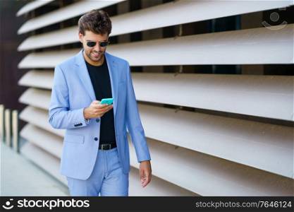 Young man walking down the street using his smartphone with a happy expression. Man walking down the street using his smartphone with a happy expression