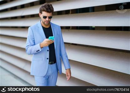 Young man walking down the street using his smartphone with a serious expression. Man walking down the street using his smartphone with a serious expression