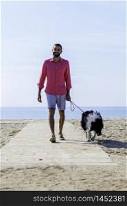 Young man walking with his dog tied up on the beach