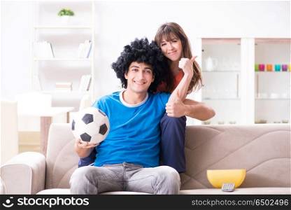 Young man watching football with his wife at home
