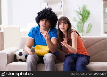 Young man watching football with his wife at home