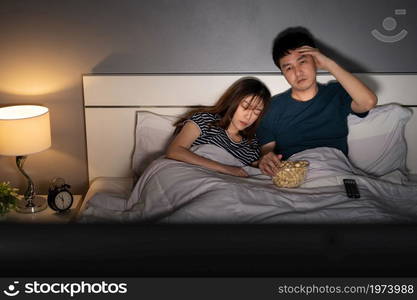 young man watching television in his bed with his wife. sleepy and tired expression suffering from insomnia