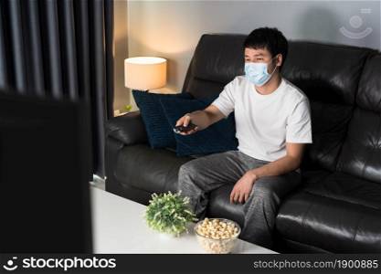 young man watching TV on sofa and wearing medical mask to protect coronavirus (Covid-19)