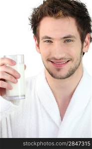 Young man wearing a bathrobe and drinking a glass of milk