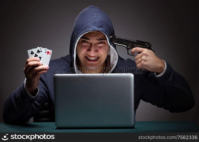 Young man wearing a hoodie sitting in front of a laptop computer gambling committing suicide. Young man wearing a hoodie sitting in front of a laptop computer