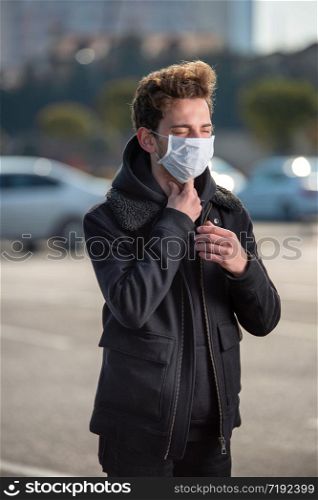 Young man wearing a mask on his face is suffering from sore throat because of the coronavirus