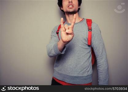 Young man wearing a red backpack is diplaying a heavy metal gesture