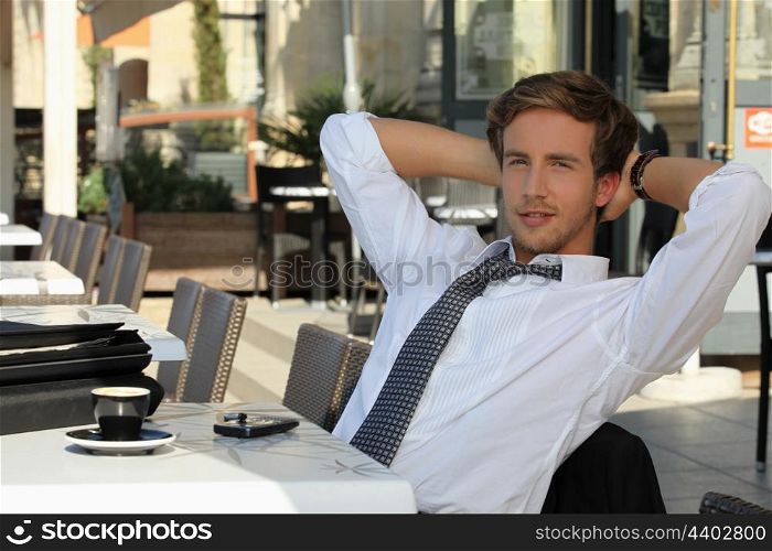 young man wearing a suit and tie, relaxing on a terrace at breakfast time