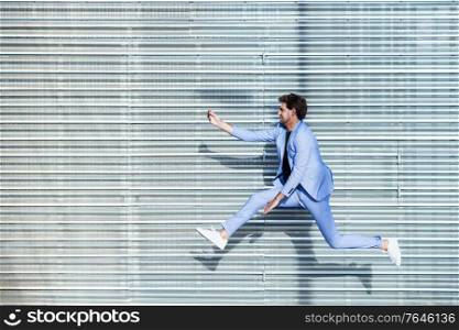 Young man wearing a suit makes a selfie with a smartphone while jumping outdoors. Man wearing a suit makes a selfie with a smartphone while jumping