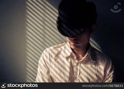 Young man wearing ahat is next to a window with shadows from blinds