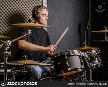 Young man wearing headphones and playing drums in a recording studio.