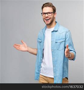 young man wearing jeans shirt welcoming you with a smile on his face and his arms wide open standing over grey background.. young man wearing jeans shirt welcoming you with a smile on his face and his arms wide open standing over grey background