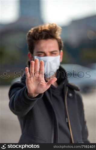 Young man wearing medical mask shows stop sign with his hand for coronavirus