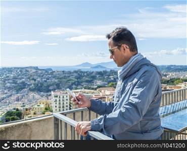 Young man wearing sunglasses standing on a terrace while using his smartphone