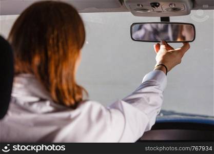 Young man wearing white shirt having long hair, driving car setting mirror inside to see better whats behind auto. Man in car looking at mirror inside