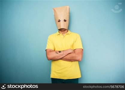 Young man with a bag over his head standing with his arms crossed