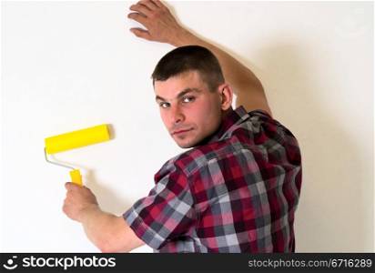 Young man with a roller in her hand is doing repair of room near wall