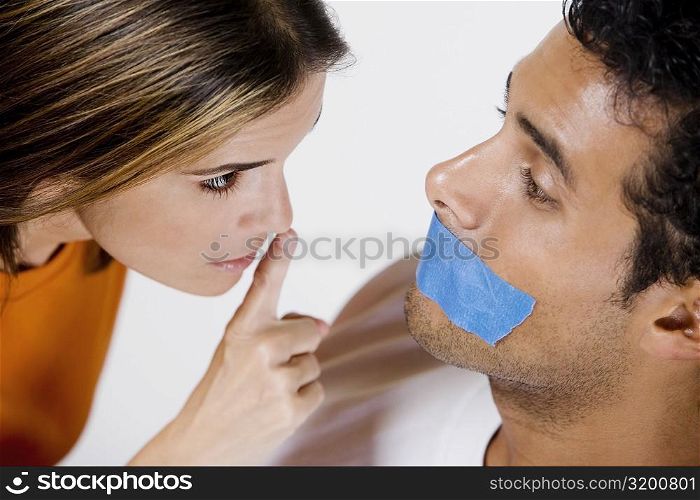Young man with adhesive tape on his mouth and mid adult woman looking at him