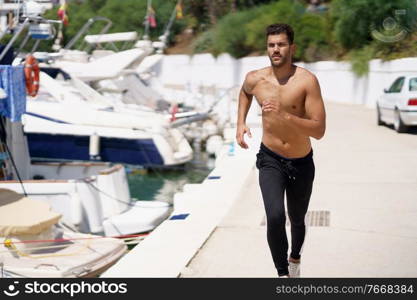 Young man with an athletic body running shirtless through a harbour full of boats.. Young man with an athletic body running shirtless through a harbour.