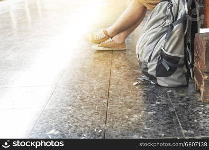 young man with backpack sitting and waiting on platform at train station - travel concept