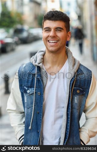 Young man with blue eyes and white teeth in the street. Model of fashion smiling in urban background wearing white t-shirt, jeans and blue jacket