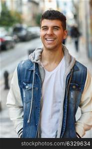 Young man with blue eyes and white teeth in the street. Model of fashion smiling in urban background wearing white t-shirt, jeans and blue jacket