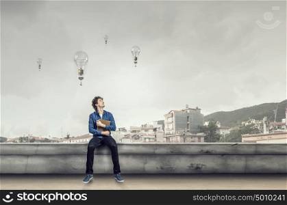 Young man with book. Guy sitting on building roof and reading book