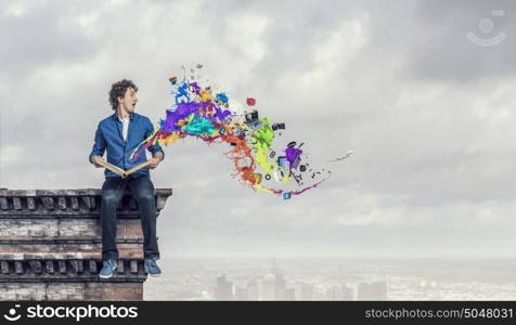 Young man with book. Guy sitting on building roof and reading book