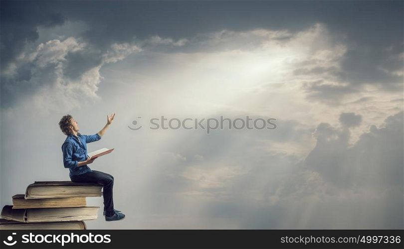 Young man with book. Guy sitting on pile of books with one in hands