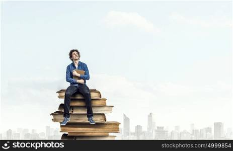 Young man with book. Guy sitting on pile of books with one in hands