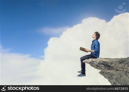 Young man with book. Guy sitting on rock edge and reading book
