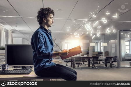 Young man with book. Guy sitting on table in modern office and reading book