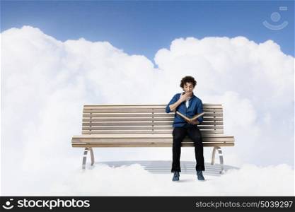 Young man with book. Guy sitting on wooden bench and reading book