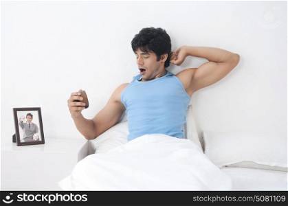 Young man with clock yawning