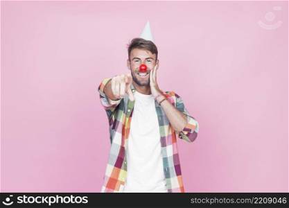 young man with clown nose pointing his finger pink background