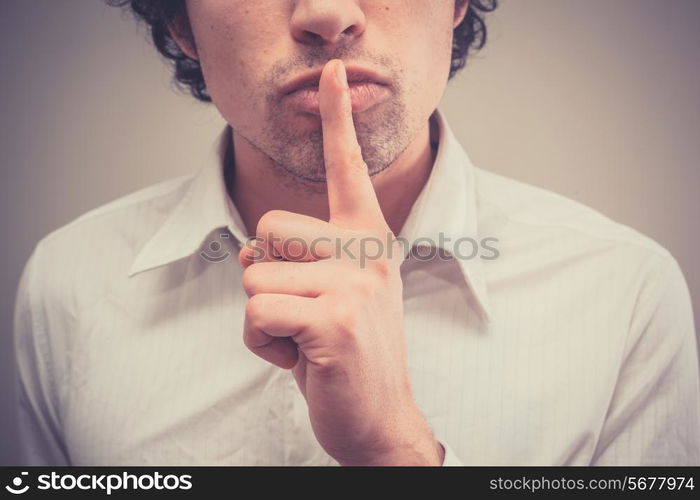 Young man with finger on lips is gesturing hush