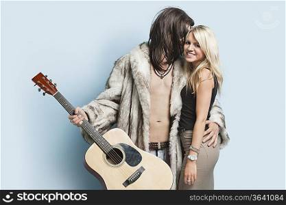Young man with guitar embracing happy woman against light blue background