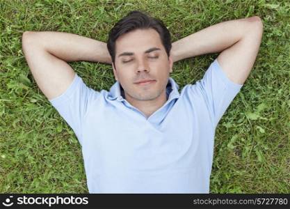 Young man with hands behind head lying on grass