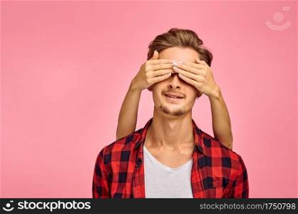 Young man with hands on his eyes, pink background, emotion. Face expression, male person looking on camera in studio, emotional concept, feelings. Young man with hands on his eyes, pink background
