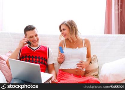 Young man with happy pregnant wife confirming online purchase by phone &#xA;