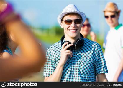 Young man with headphones. Image of young man with friends at background. Summer vacation