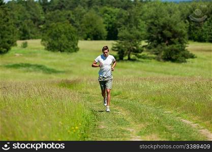 Young man with headphones jogging in a meadow, shallow DOF